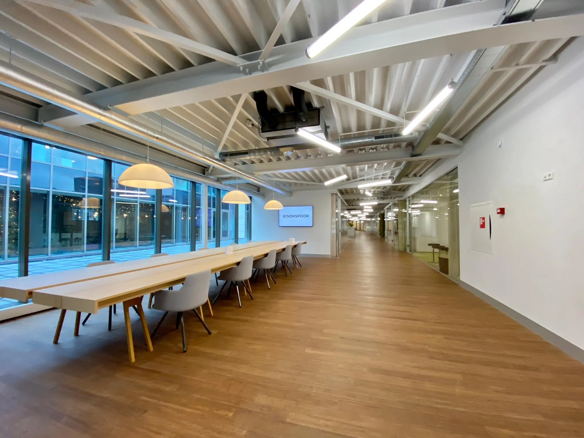 Moderne kantoorruimte met lange houten tafel, designstoelen en het logo van Bisonspoor op een scherm aan de muur.