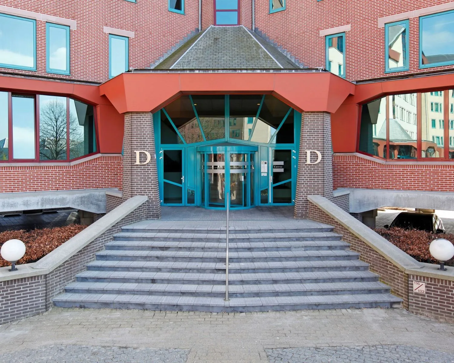 Hoofdentree van gebouwdeel D met trap, glazen deur en rood-bruin metselwerk.