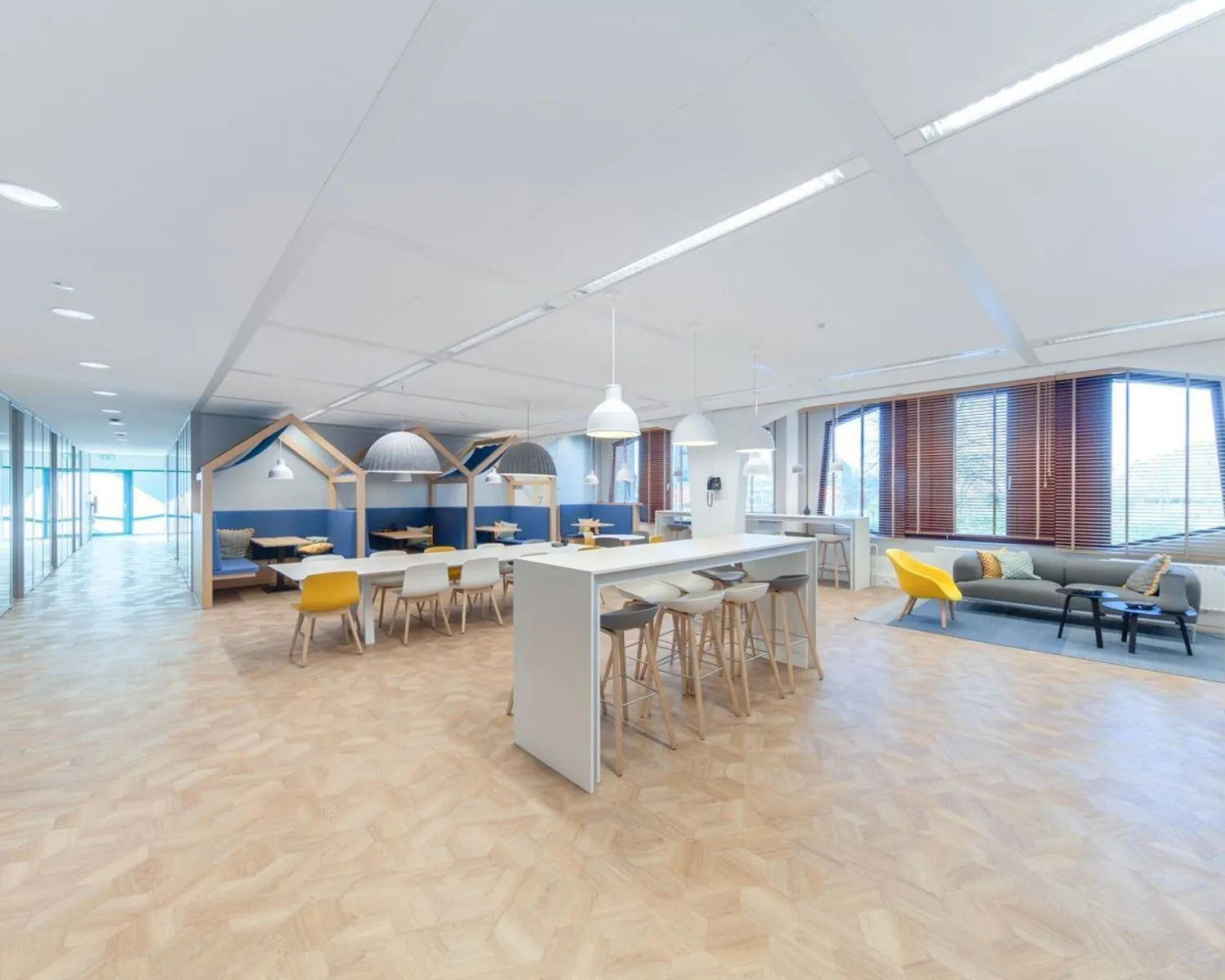 Moderne, open kantoorruimte met zithoeken, lange werktafels en natuurlijke lichtinval.