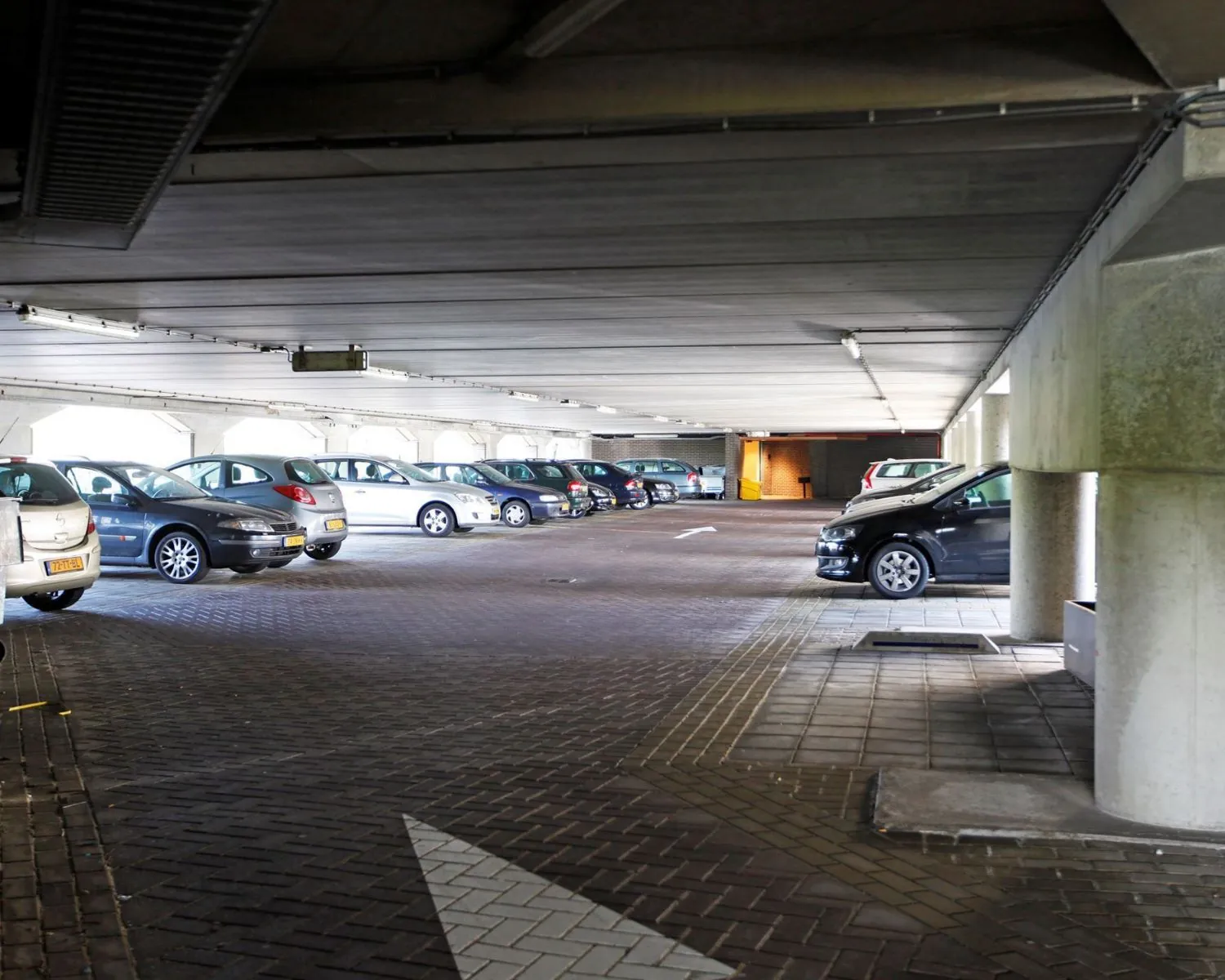 Ondergrondse parkeergarage met geparkeerde auto's in twee rijen en een pijl op de vloer die de rijrichting aangeeft.