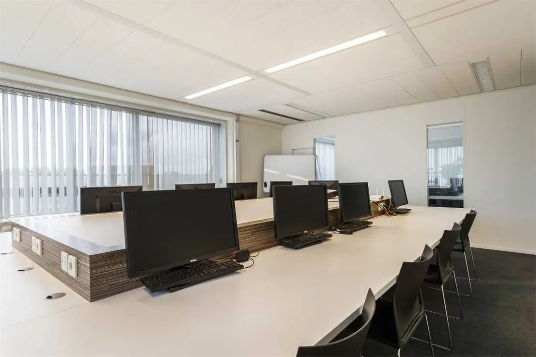 Moderne kantoorruimte aan de Savannahweg met werkplekken voorzien van computers en grote ramen met verticale jaloezieën.