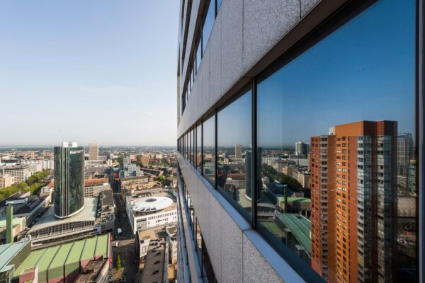 Uitzicht vanaf een hoog gebouw op de Blaak in Rotterdam met weerspiegeling van de stad in de glazen gevel.