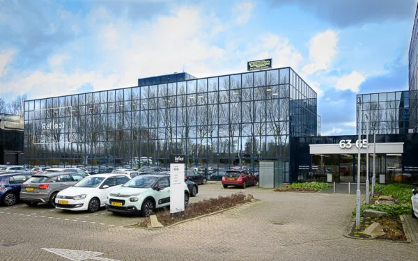 Glazen kantoorgebouw Refleqt aan de Essebaan 63-65 met parkeerterrein vol geparkeerde auto's.