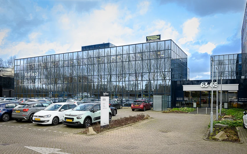 Glazen kantoorgebouw Refleqt aan de Essebaan 63-65 met parkeerterrein vol geparkeerde auto's.