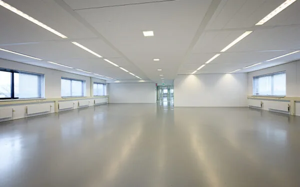 Lege kantoorruimte aan de Essebaan met strakke witte wanden, grijze vloer en grote ramen.