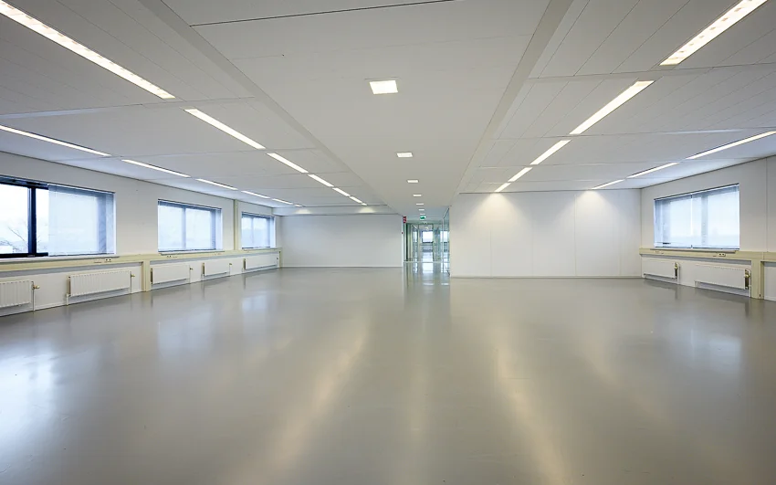 Lege kantoorruimte aan de Essebaan met strakke witte wanden, grijze vloer en grote ramen.
