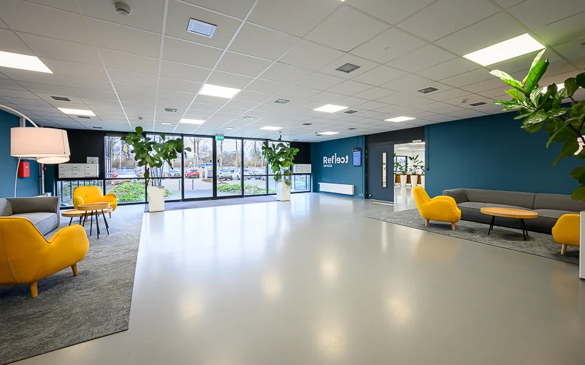Moderne, lichte ontvangsthal van Refleqt Offices met gele stoelen, grijze banken en grote planten.