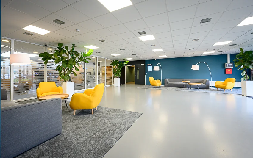 Moderne en lichte wachtruimte met gele fauteuils, grijze banken, planten en sfeerverlichting in kantoorpand Essebaan.