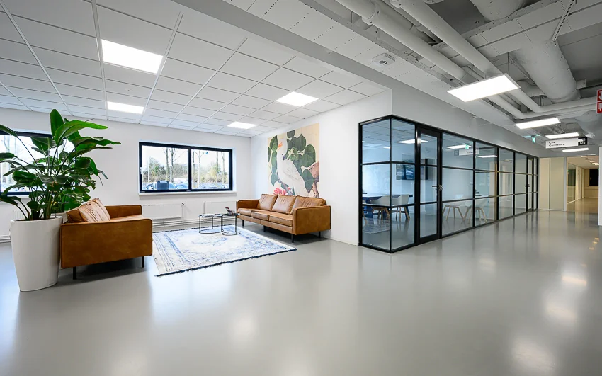 Moderne wachtruimte met twee cognackleurige banken, een groot schilderij, een vloerkleed en een glazen vergaderruimte in een kantoor aan de Essebaan.