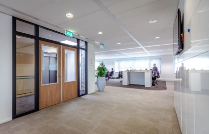 Kantoorruimte aan de Contactweg met bureaus, mensen aan het werk en een glazen ingang met dubbele deur.