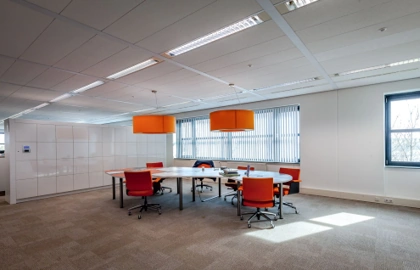 Vergaderruimte aan de Contactweg met een grote tafel, rode stoelen en opvallende oranje lampen.