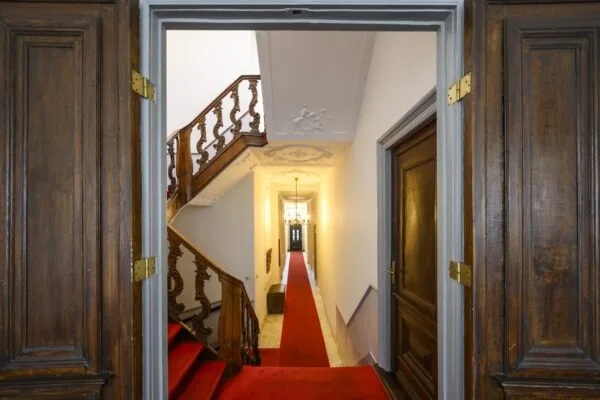 Doorkijk in een karakteristiek grachtenpand aan de Keizersgracht met een houten trap, sierplafond en rode loper in de gang.