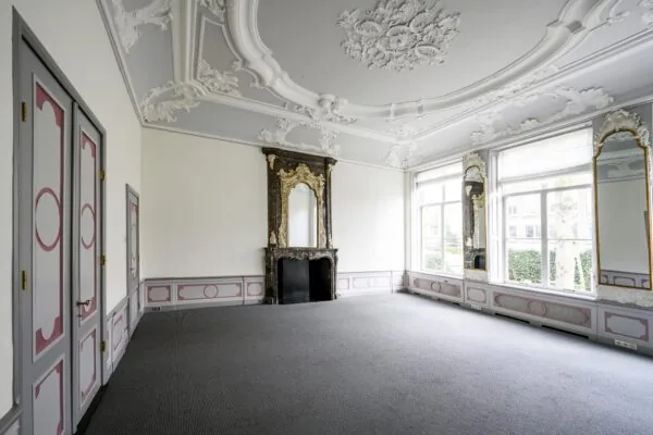 Lichte, klassiek ingerichte kamer aan de Keizersgracht met ornamentenplafond, marmeren schouw en grote spiegels bij hoge ramen.