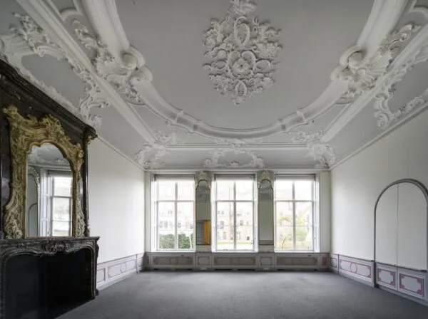 Klassiek interieur van een kamer aan de Keizersgracht met rijk gedecoreerd stucplafond, hoge ramen en een sierlijke schouw met spiegel.