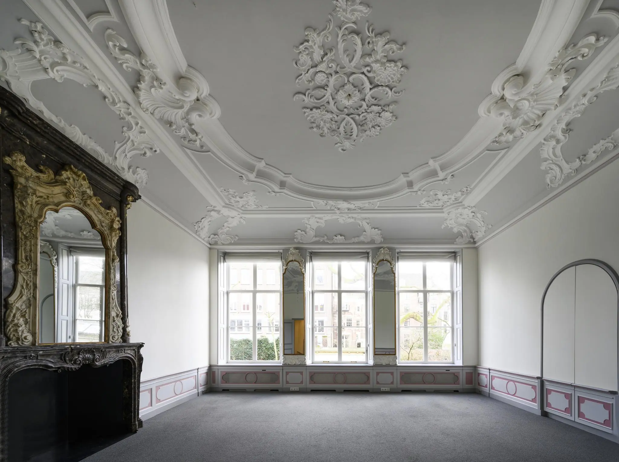 Klassiek interieur van een kamer aan de Keizersgracht met rijk gedecoreerd stucplafond, hoge ramen en een sierlijke schouw met spiegel.