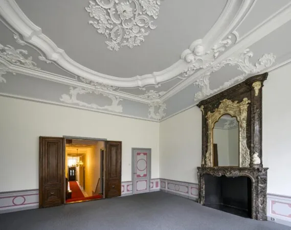 Sierlijke kamer aan de Keizersgracht met rijk gedecoreerd stucplafond en monumentale schouw met spiegel.