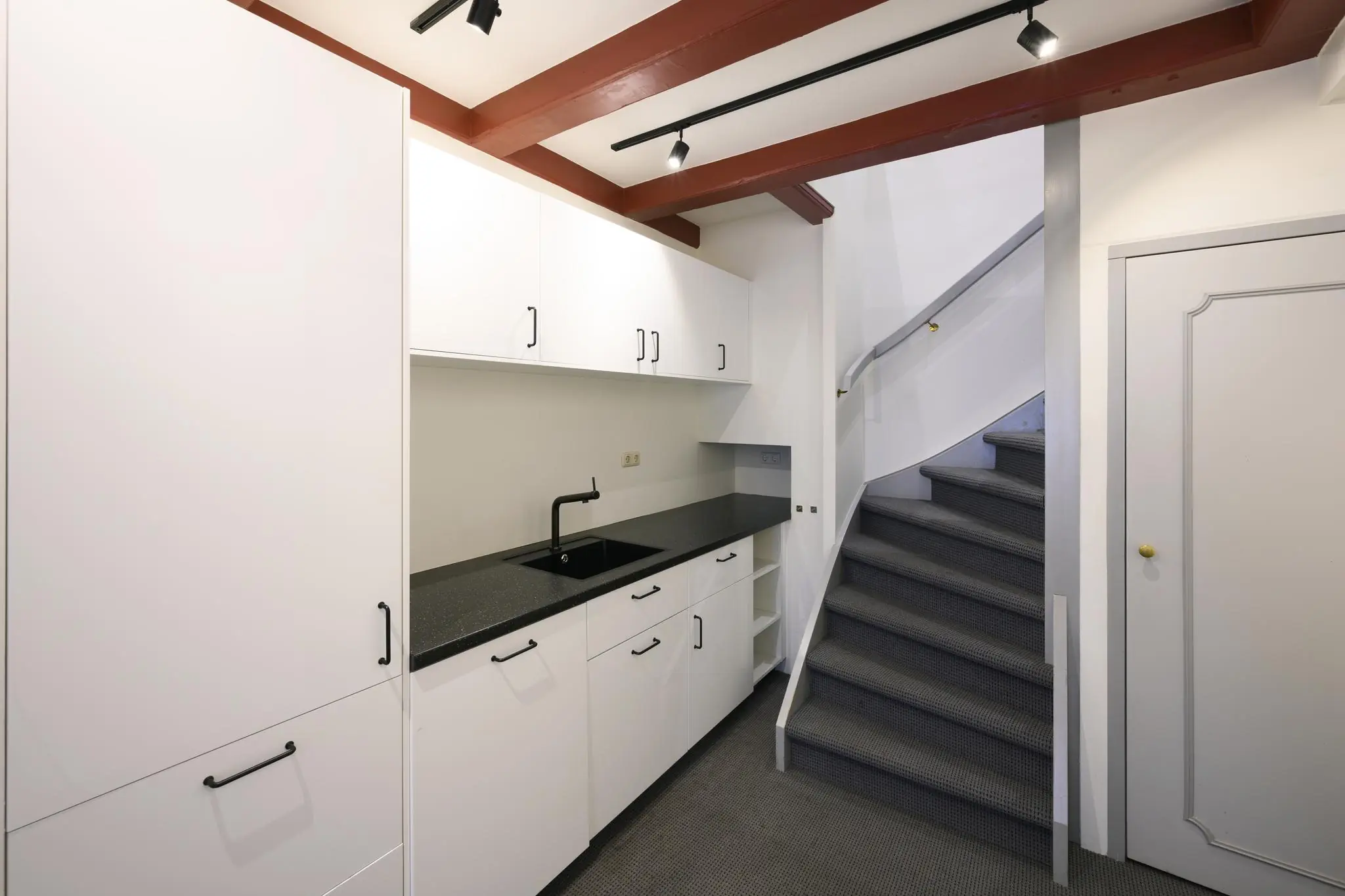 Moderne kitchenette met witte kasten, zwart aanrechtblad en een tapijtbeklede trap in een appartement aan de Keizersgracht.
