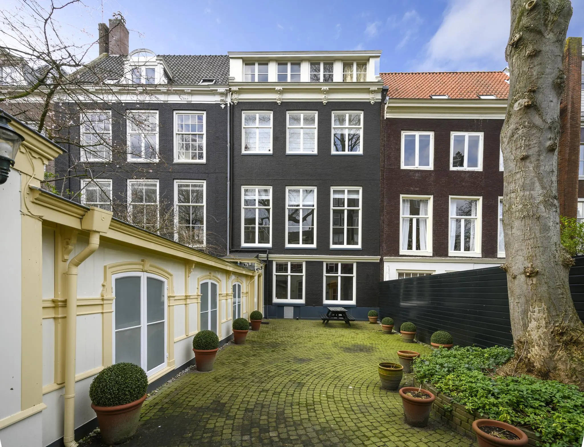 Binnenplaats met planten en uitzicht op klassieke grachtenpanden aan de Keizersgracht in Amsterdam.