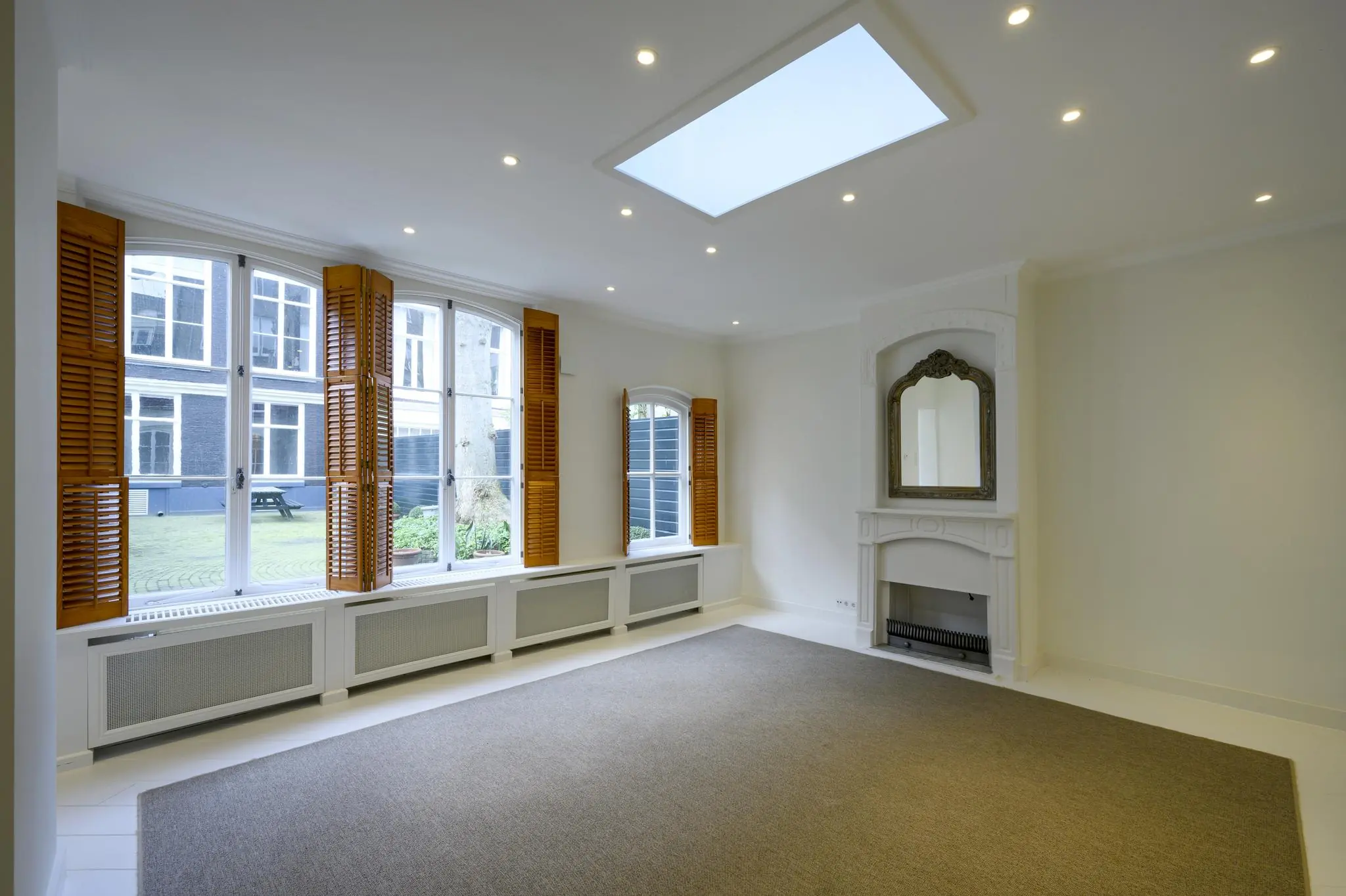Licht en ruim interieur aan de Keizersgracht met grote ramen, houten shutters, een sierlijke schouw en een dakraam.