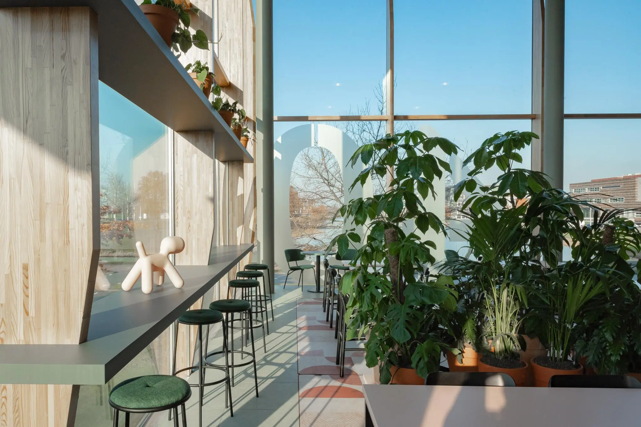 Lichte, moderne zithoek aan de Hondiuslaan met hoge ramen, veel groen en houten accenten.