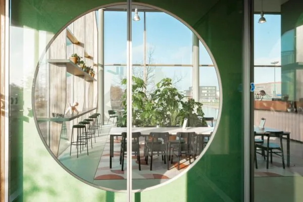 Modern interieur van een lichte vergaderruimte aan de Hondiuslaan, gezien door een groot rond raam met uitzicht op groen en strak meubilair.