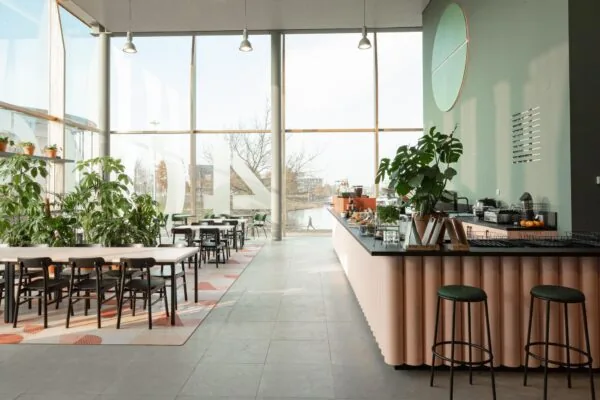 Moderne en lichte horecaruimte aan de Hondiuslaan met grote ramen, veel planten en een uitnodigende koffiebar.