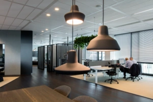 Moderne kantoorruimte aan de Herikerbergweg met werkplekken, hanglampen en twee personen aan een bureau.