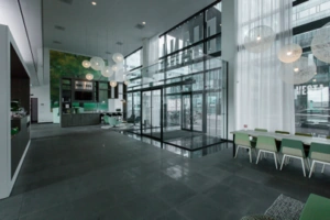 Moderne, ruime ontvangsthal van een kantoorpand aan de Herikerbergweg met glazen entree, zithoek en groene accenten.