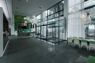 Moderne, ruime ontvangsthal van een kantoorpand aan de Herikerbergweg met glazen entree, zithoek en groene accenten.