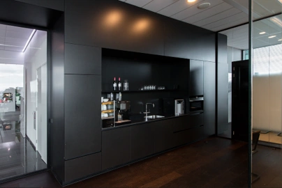 Moderne, zwarte kantoorkeuken met ingebouwde koffiemachine en glazen opbergplanken aan de Herikerbergweg.