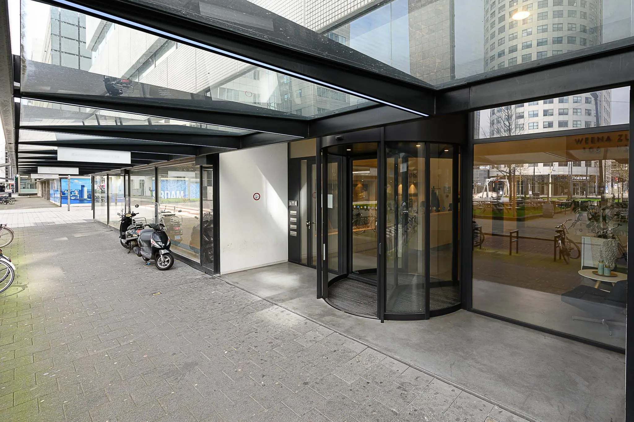 Ingang van een modern kantoorgebouw aan het Weena-Zuid met glazen deuren en overkapping.