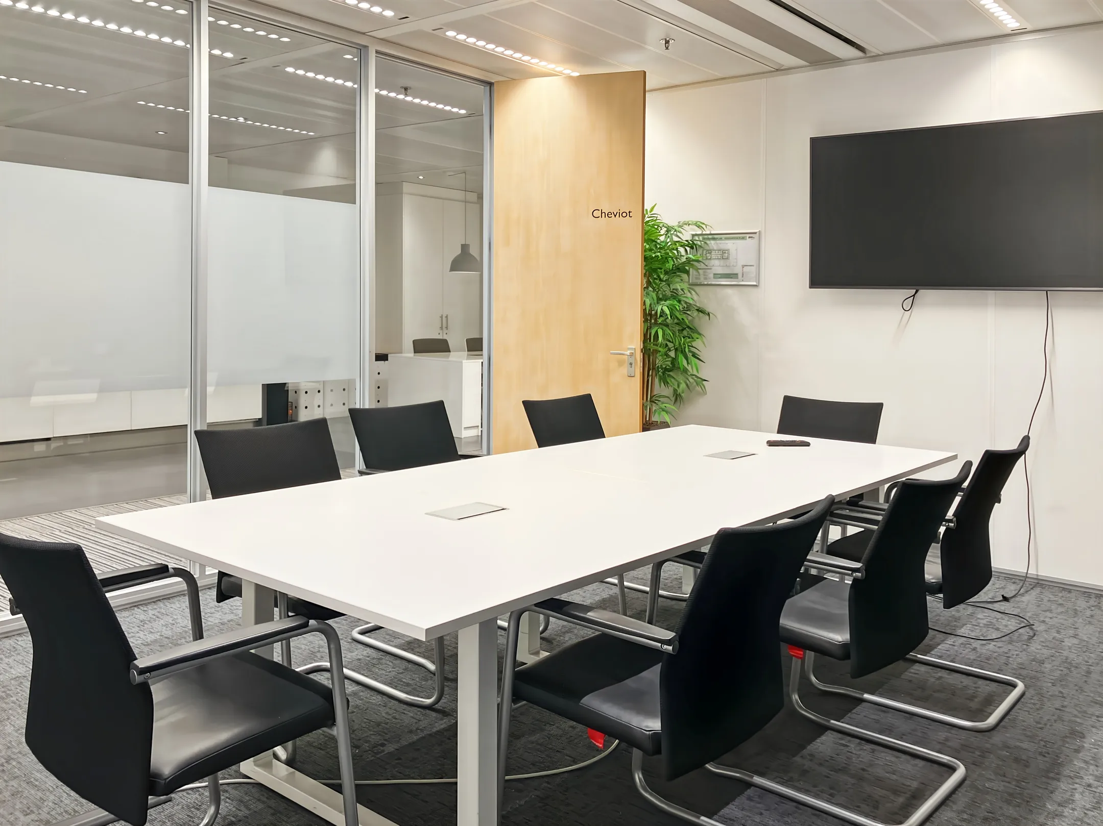 Een moderne vergaderruimte met een witte tafel, zwarte stoelen, een groot beeldscherm aan de muur en een deur met het opschrift "Cheviot".