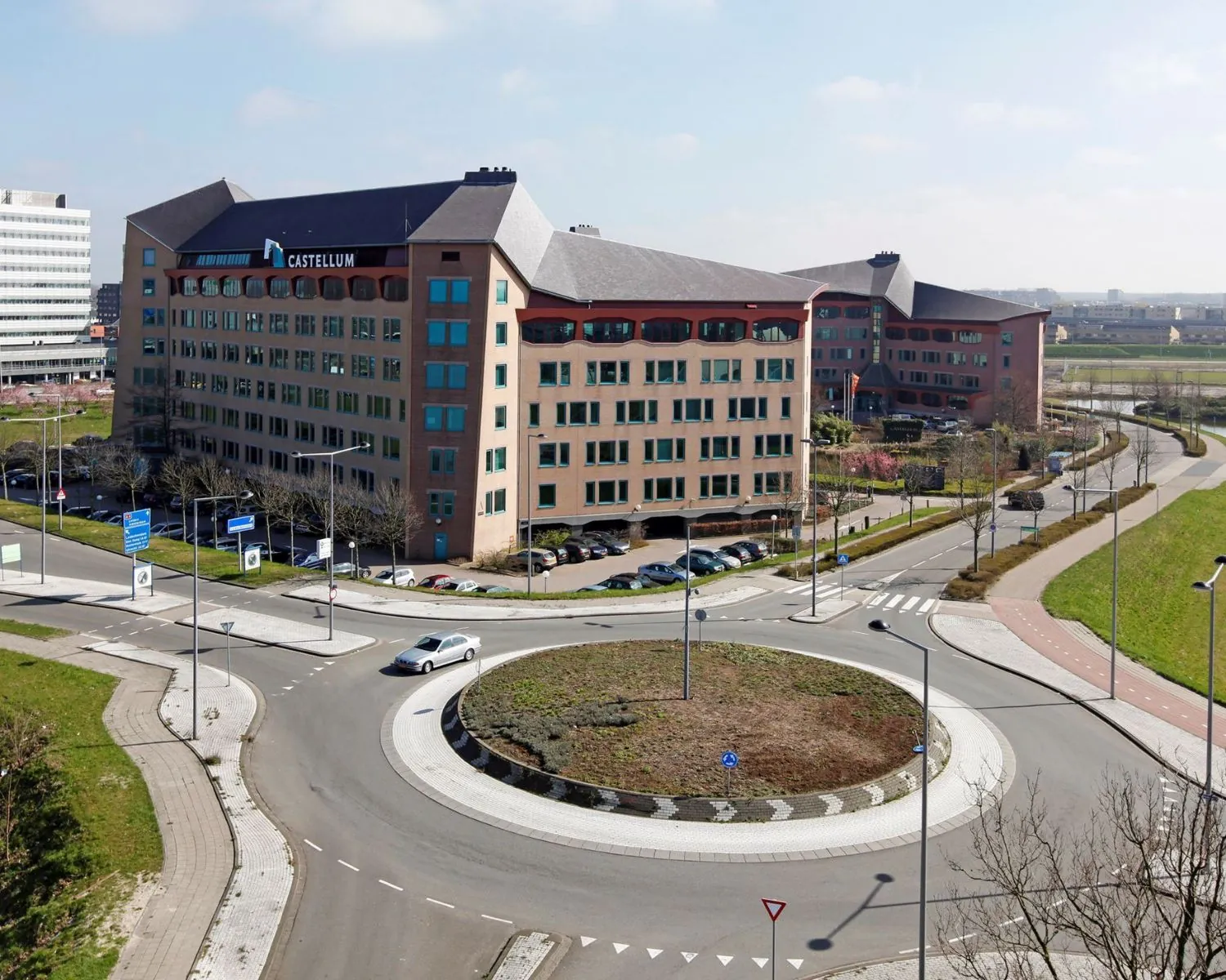 Kantoorgebouw Castellum aan een rotonde met omliggende wegen en parkeerplaatsen.