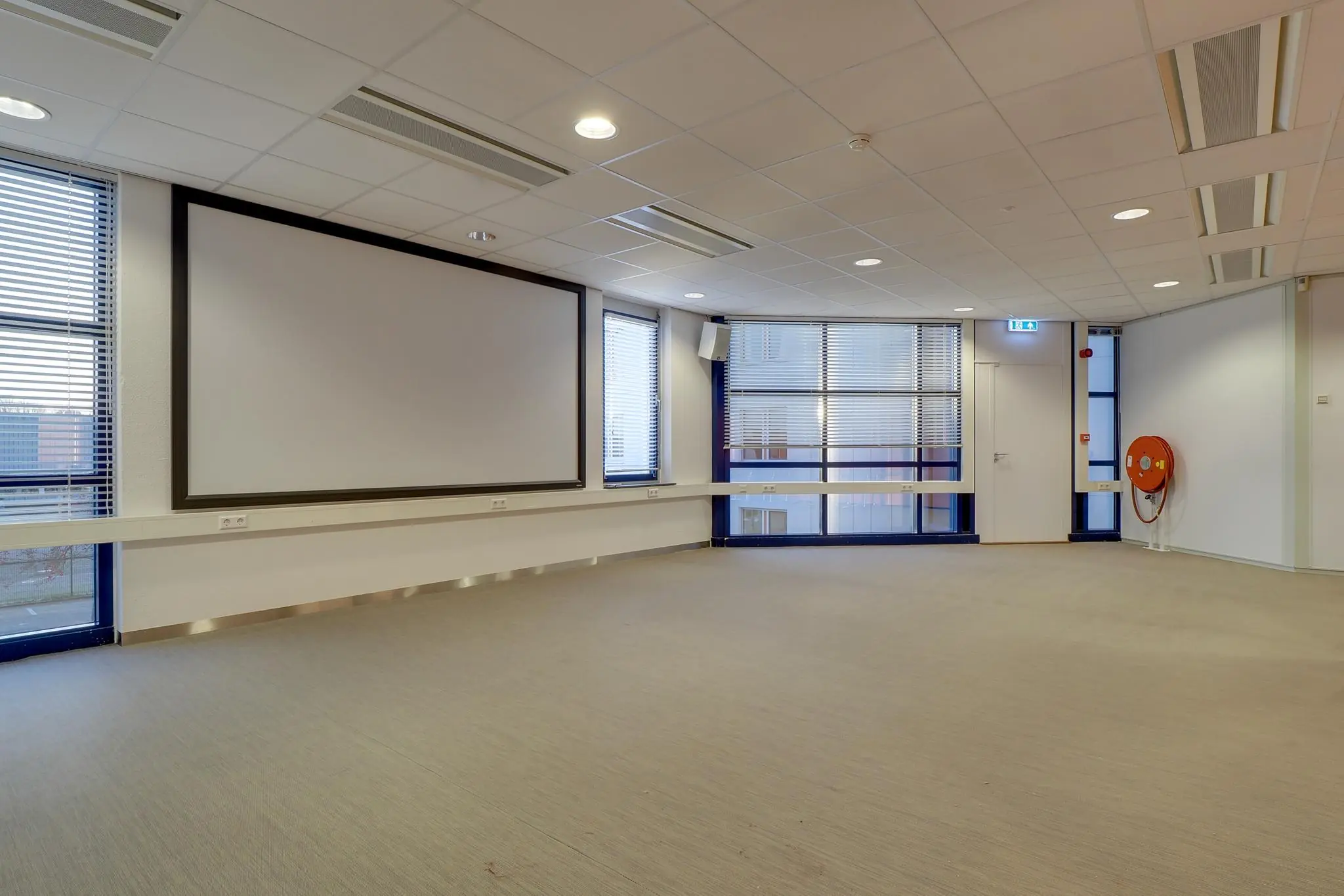 Lege vergaderruimte in Rijnzathe met groot projectiescherm en blinderende ramen.