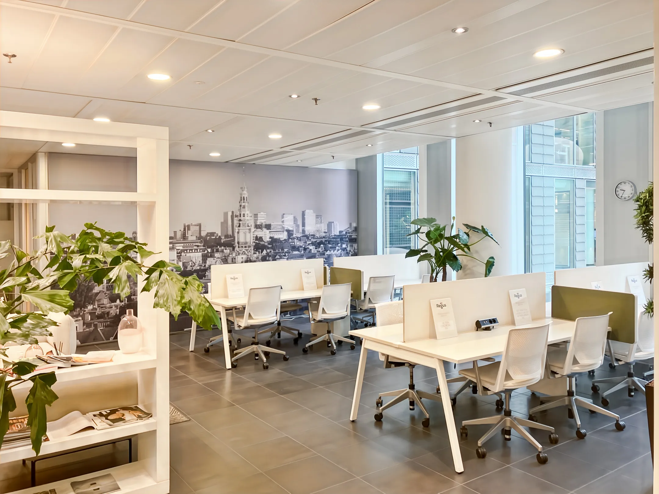 Een moderne kantoorruimte met bureaus, stoelen en planten, met een fotobehang van een stadsgezicht op de achtergrond.