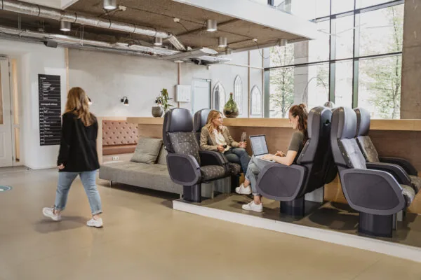 Twee vrouwen werken en praten in een moderne lounge met treinachtige stoelen in HNK Utrecht CS.