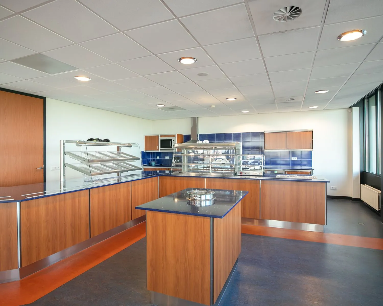 Moderne bedrijfskeuken met houten kasten, glazen vitrines en blauwe accenten in een kantoorruimte aan de Carlsonstraat 13 in Kampen.