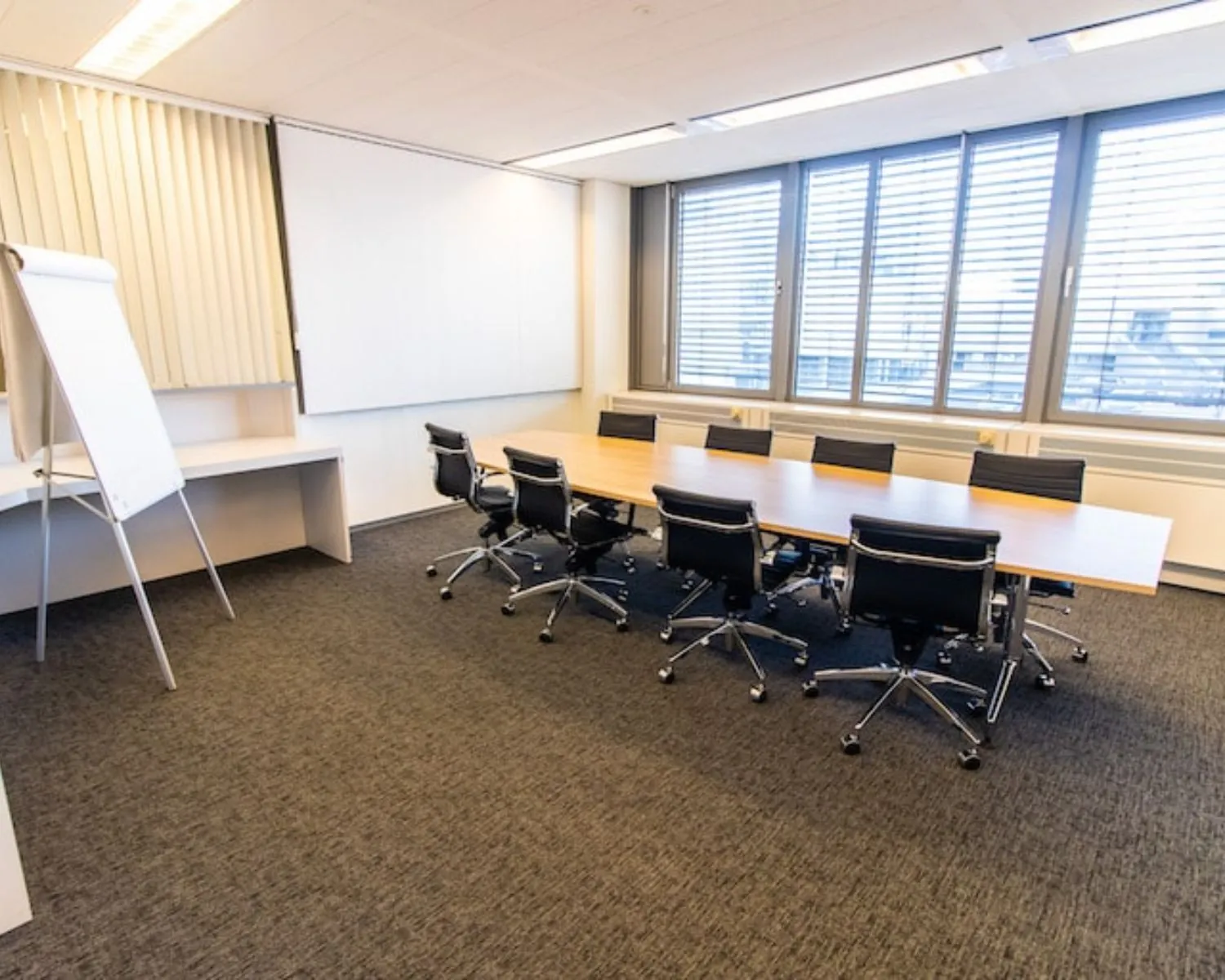 Vergaderruimte met lange tafel, zwarte stoelen en flip-over in een kantoor aan de Gaetano Martinolaan 75-95 in Maastricht.