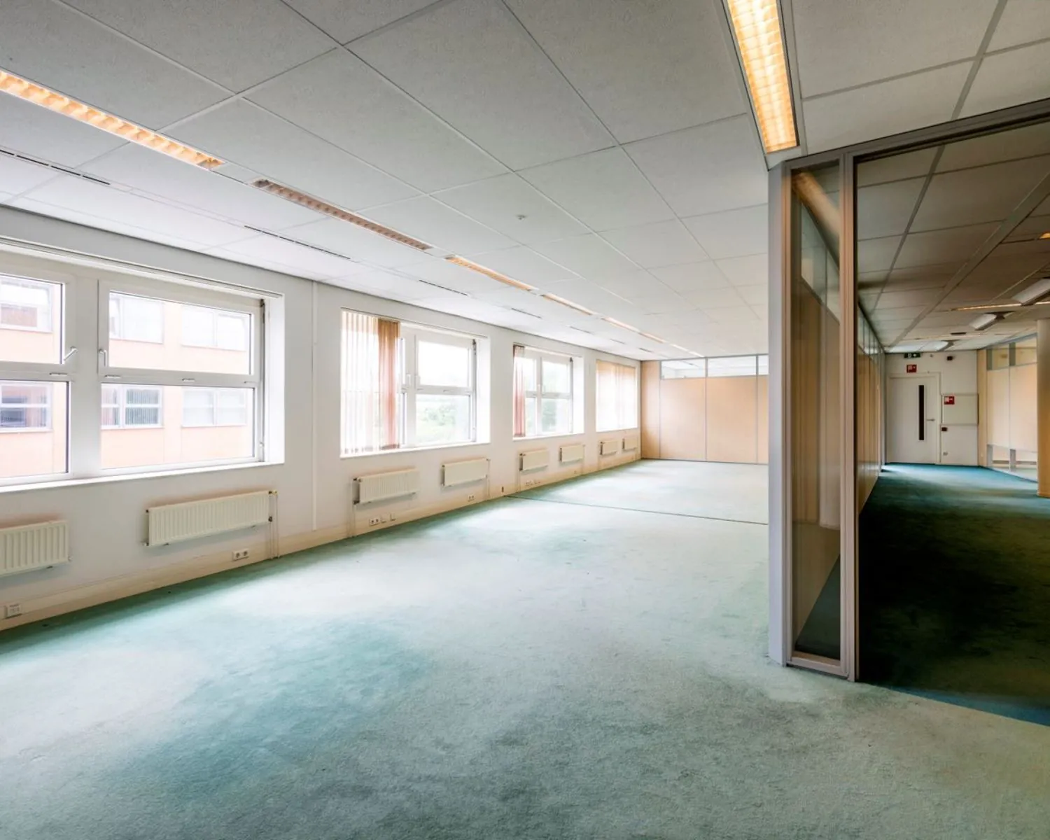 Lichte, lege kantoorruimte met tapijt en grote ramen aan de Entrada 300 in Amsterdam.