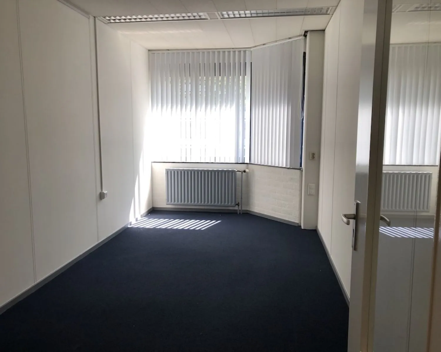 Lichte, lege kantoorruimte met tapijtvloer en verticale lamellen aan de Hooilaan 1 in Breda.