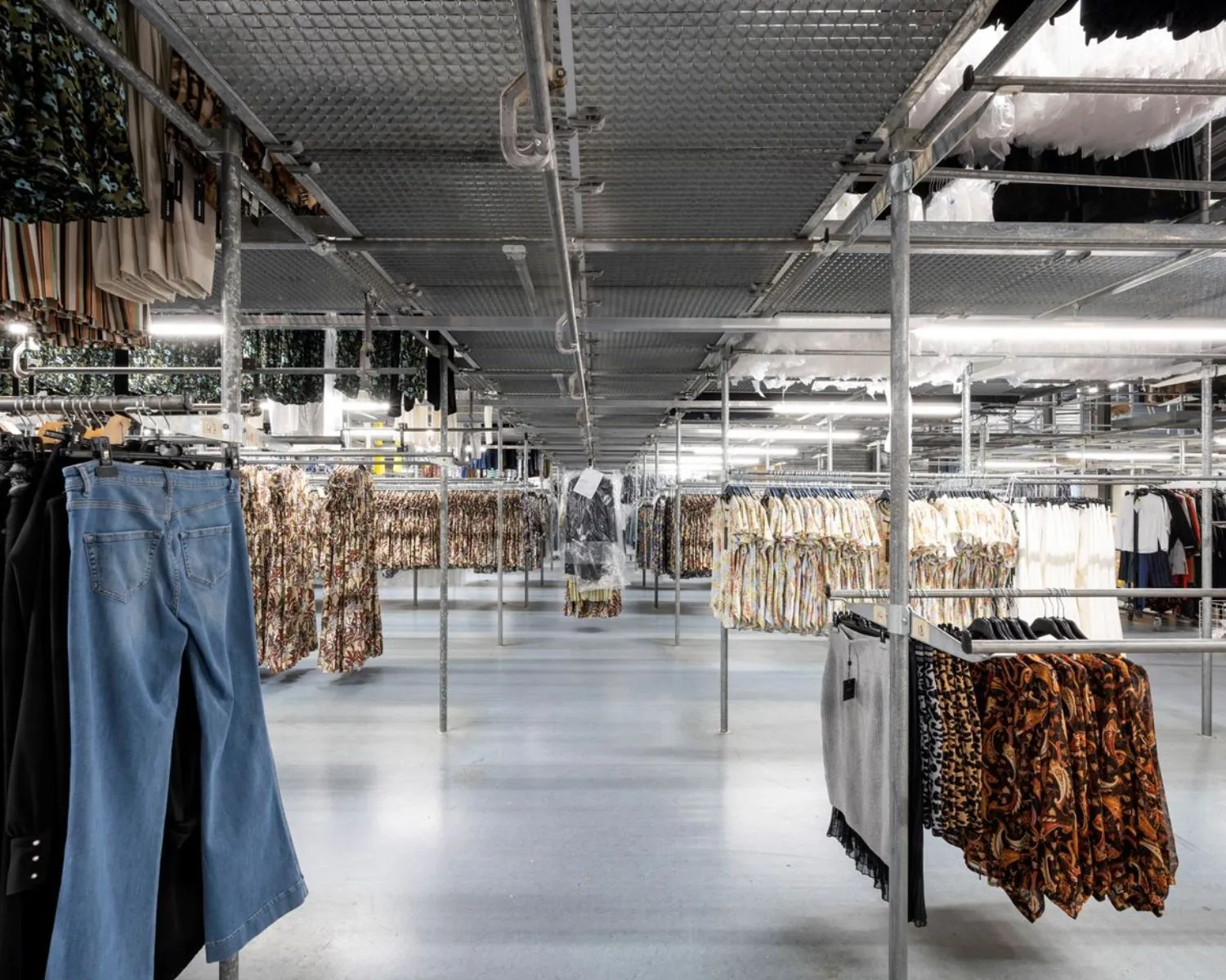 Ruime kledingopslag met metalen rekken en hangende kledingstukken in een bedrijfsruimte aan de Stammerhove 1 in Diemen.