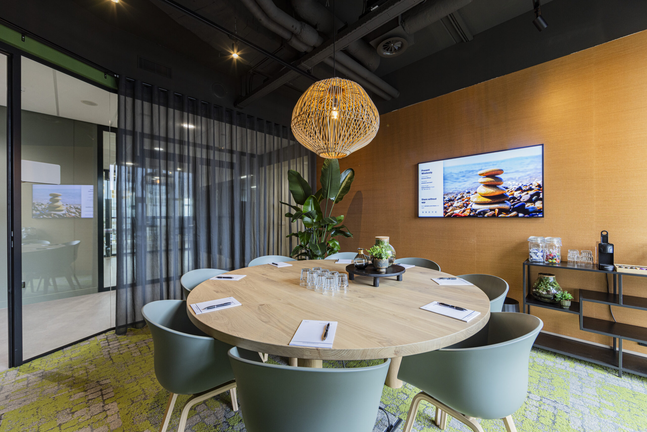 Moderne vergaderruimte in Rotterdam met een ronde houten tafel, groene stoelen, planten en een scherm aan de muur.