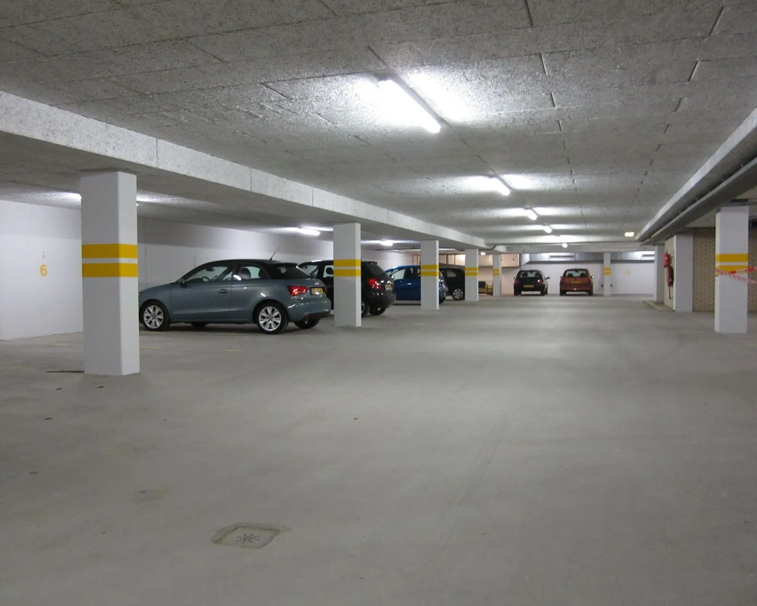 Ondergrondse parkeergarage met meerdere geparkeerde auto's en betonnen pilaren.