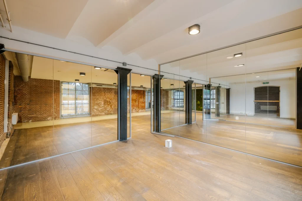 Een lege ruimte met houten vloer, bakstenen muren en grote spiegels.