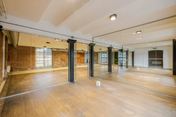 Een lege ruimte met houten vloer, bakstenen muren en grote spiegels.