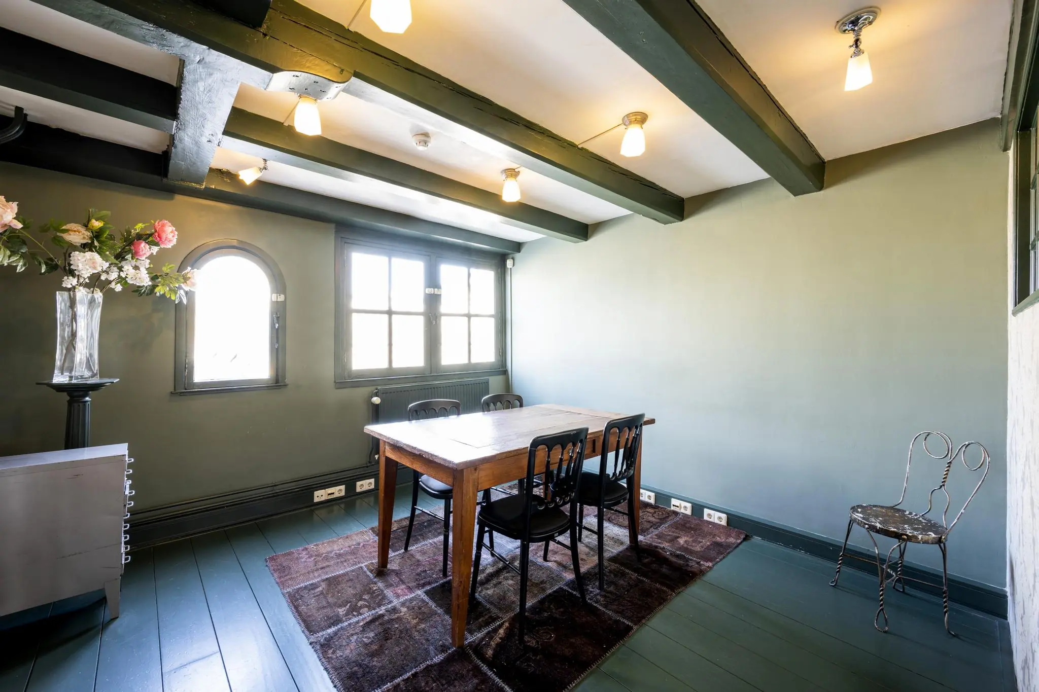 Licht ingerichte vergaderruimte aan de Leidsegracht met houten tafel, zwarte stoelen en bloemenvaas bij een boograam.