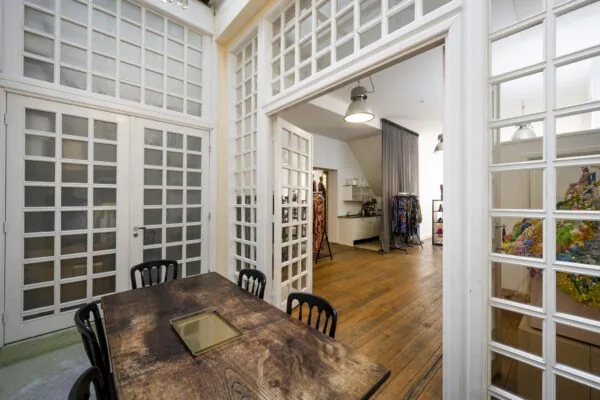 Interieur van een licht appartement aan de Leidsegracht met houten vloer, glazen paneeldeuren en zicht op een eet- en werkruimte.