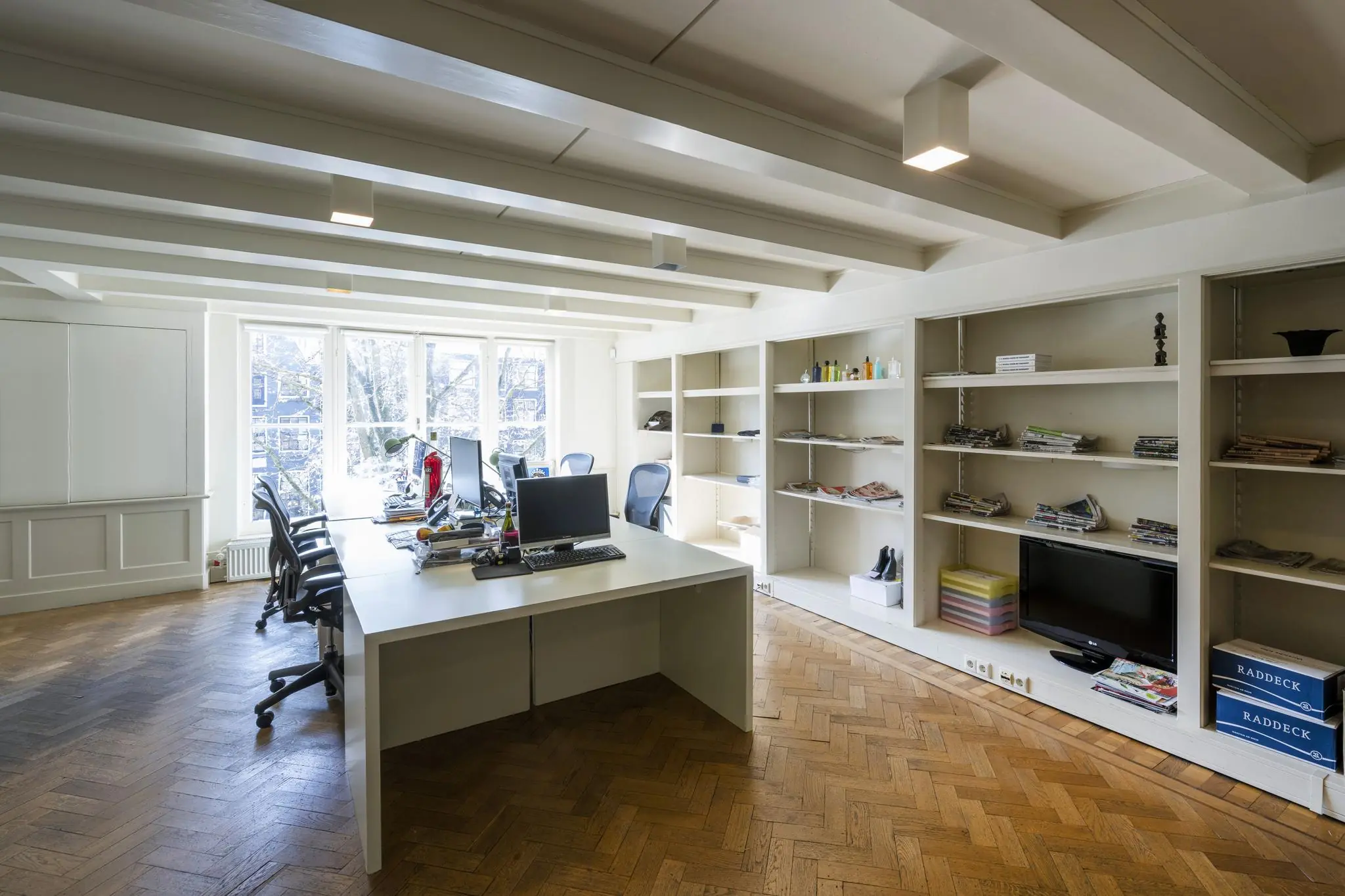 Modern kantoorinterieur aan de Leidsegracht met houten vloer, bureaus en open wandkasten.
