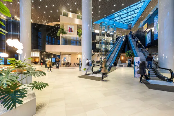 Modern interieur van kantoorgebouw aan het Weena met roltrappen, glazen liften en bezoekers in beweging.