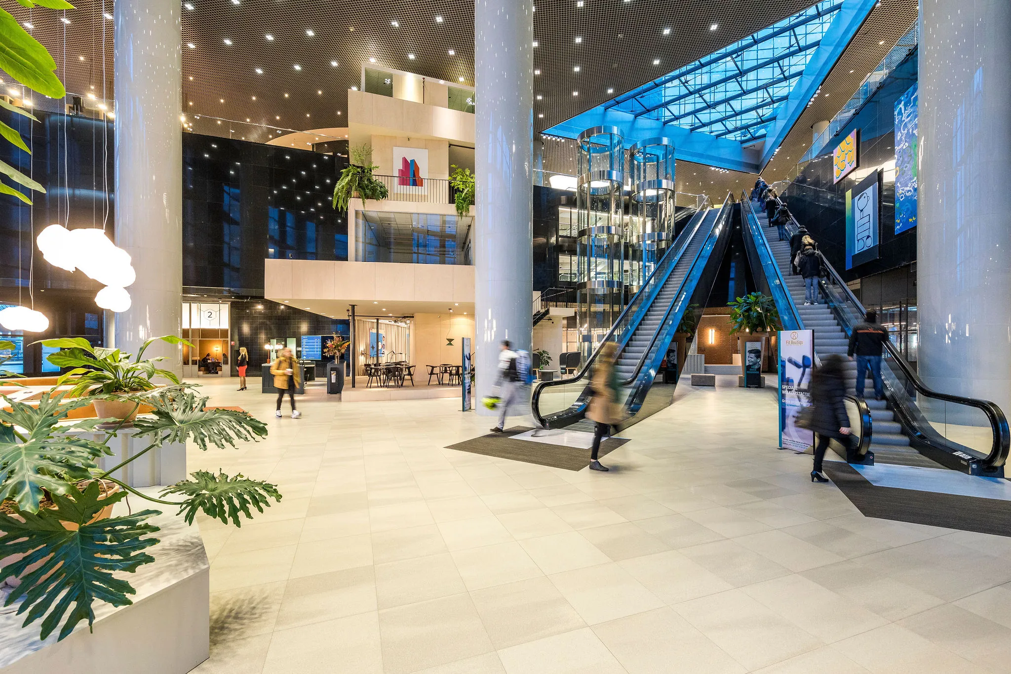 Modern interieur van kantoorgebouw aan het Weena met roltrappen, glazen liften en bezoekers in beweging.